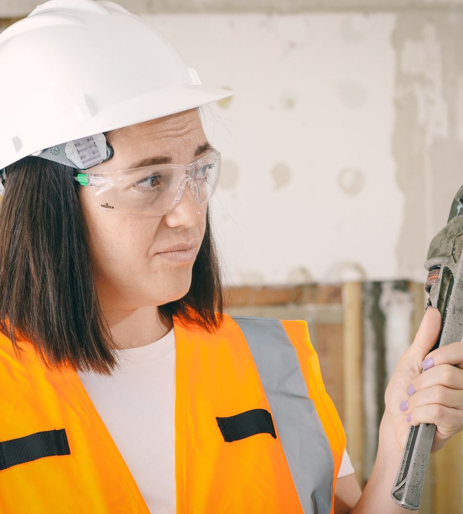A Frontline plumber in safety gear holding a pipe wrench, ready for a service call